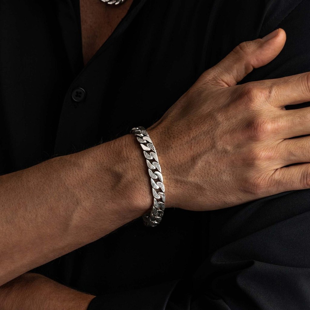 Man in a black shirt with his hand on his chest, wearing the Ronatelli Athena 9 mm Greek key curb 925 sterling silver bracelet
