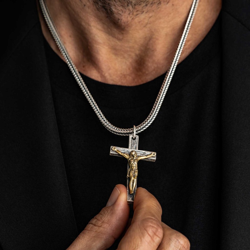 Man in a black T-shirt holding the Ronatelli Cascia 925 sterling silver crucifix pendant, a gold-tone figure on an oxidized cross, on a foxtail chain