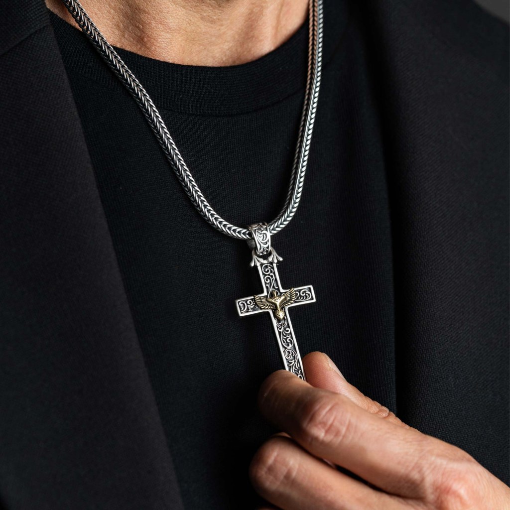 A man in a black T-shirt and jacket holding up the Ronatelli Cervia eagle cross 925 sterling silver pendant on a foxtail chain