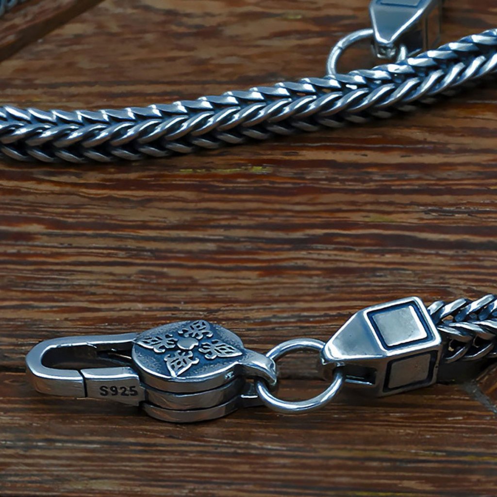 Close-up of the Ronatelli Sergo 4 mm foxtail chain: the darkened V-shaped weave, a square end cap wider than the chain, a closed ring, and a lobster clasp with an engraved disc stamped S925